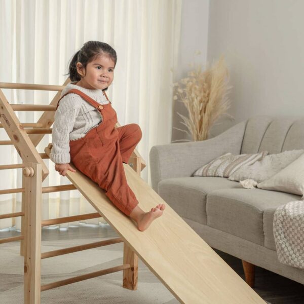 Niña pequeña usando triángulo Pikler Montessori con rampa para desarrollar equilibrio y movimiento en casa