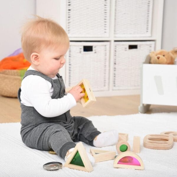Bebé explorando bloques sensoriales de madera con ventanas de colores Montessori en suelo