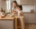 niña usando torre de aprendizaje Montessori en cocina participando en preparación de alimentos con su madre