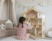 Niña jugando con casa de muñecas Montessori de madera en dormitorio infantil diseñado para fomentar imaginación, autonomía y juego creativo